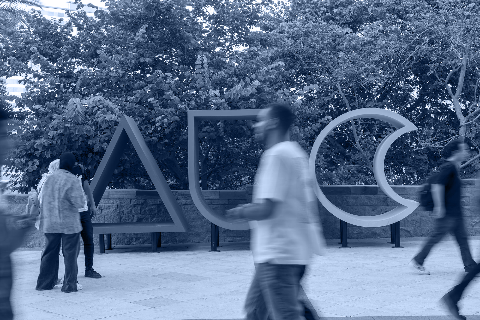 Physics Diploma Monotone image of students walking past AUC logo on campus
