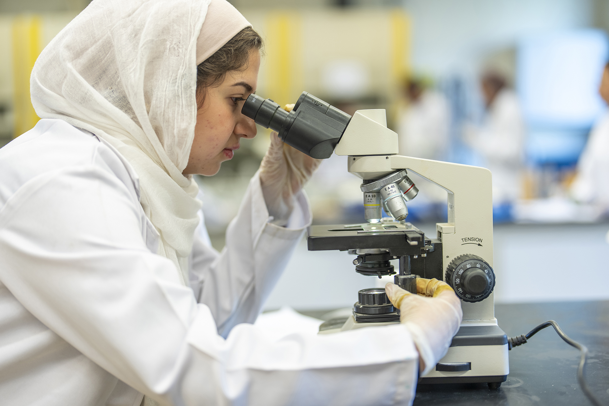 student working with microscope equipment in science lab wearing white coat