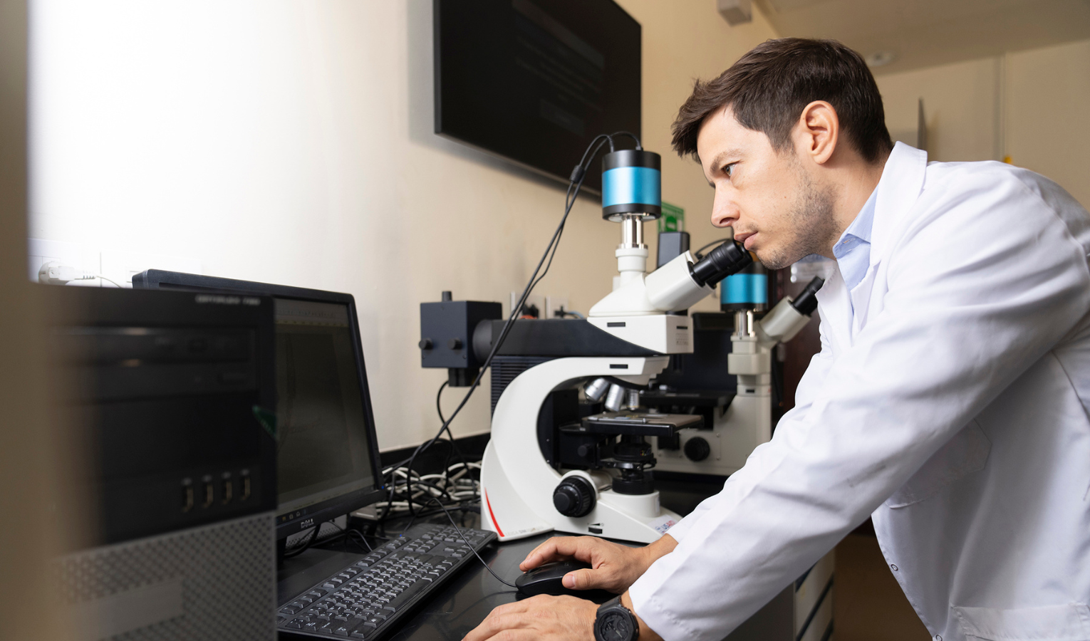 A scientist in a lab coat peers through a microscope.