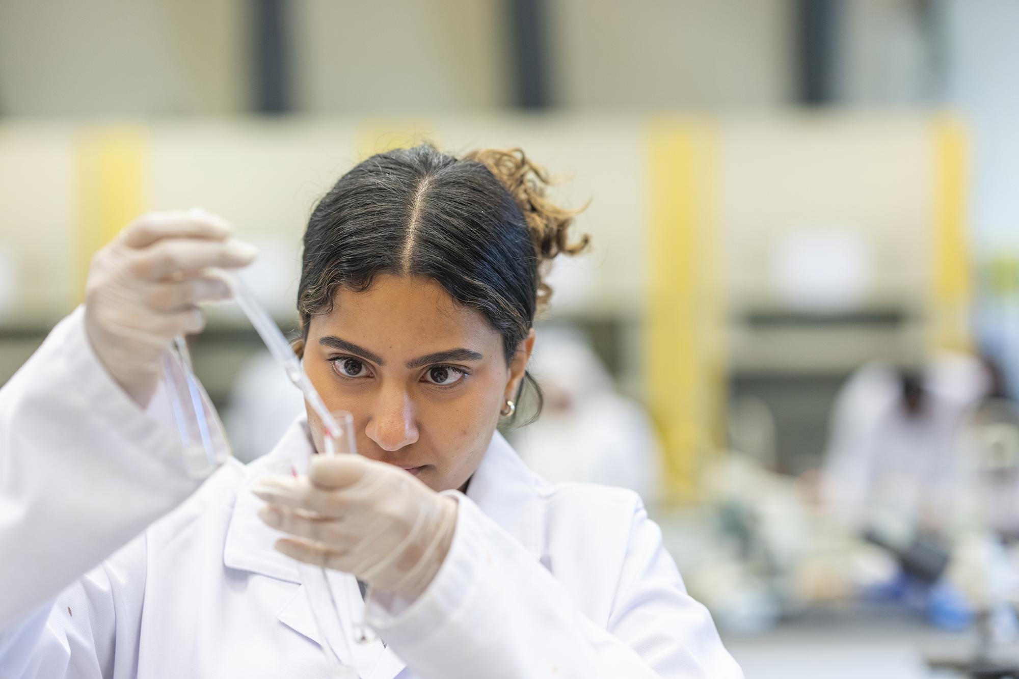 female student in lab coat working with chemical equipment in lab