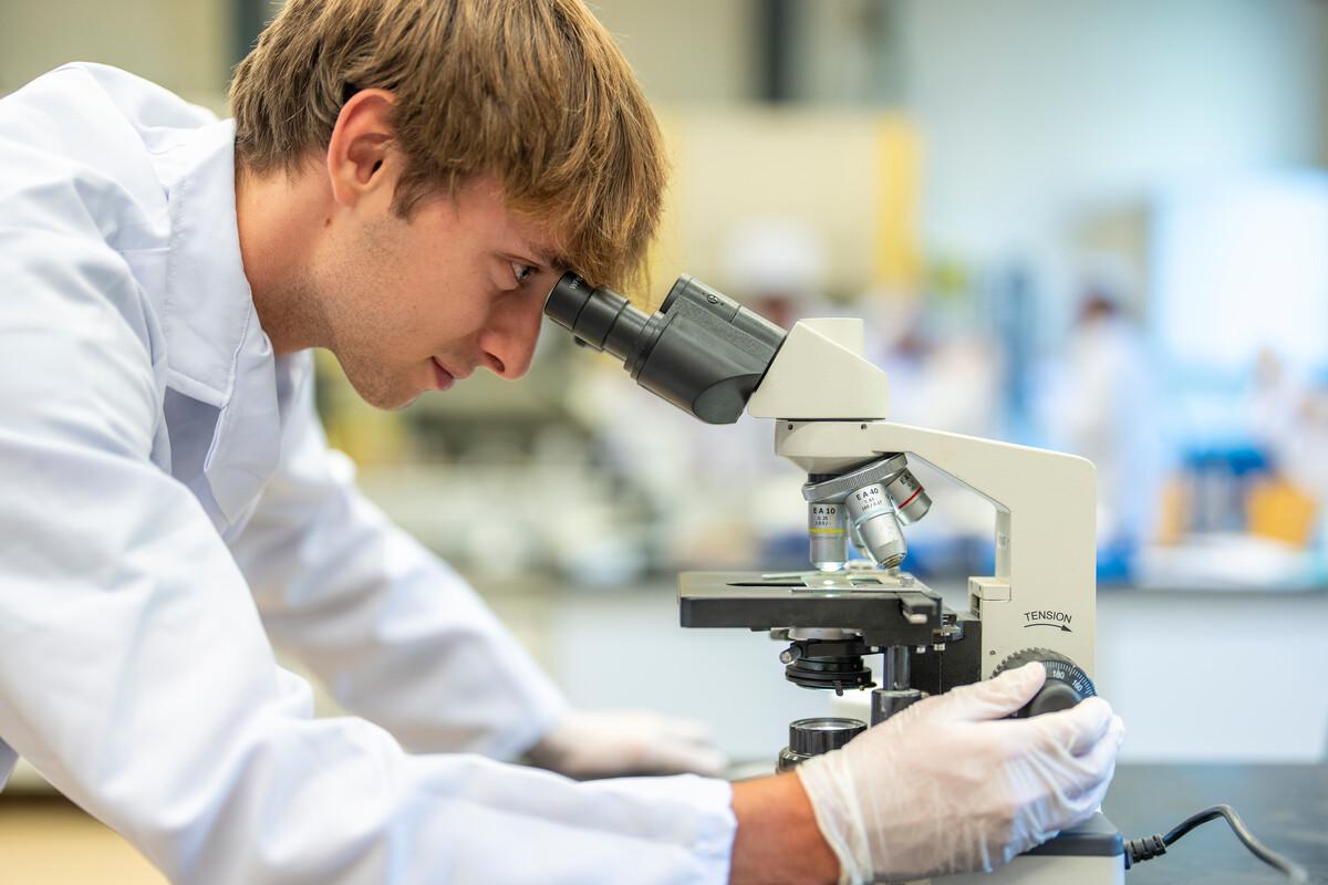 student working wearing white lab coat inside lab working with a microscope