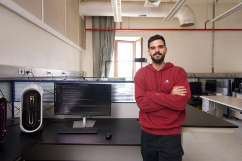 A male is standing in a lab and smiling