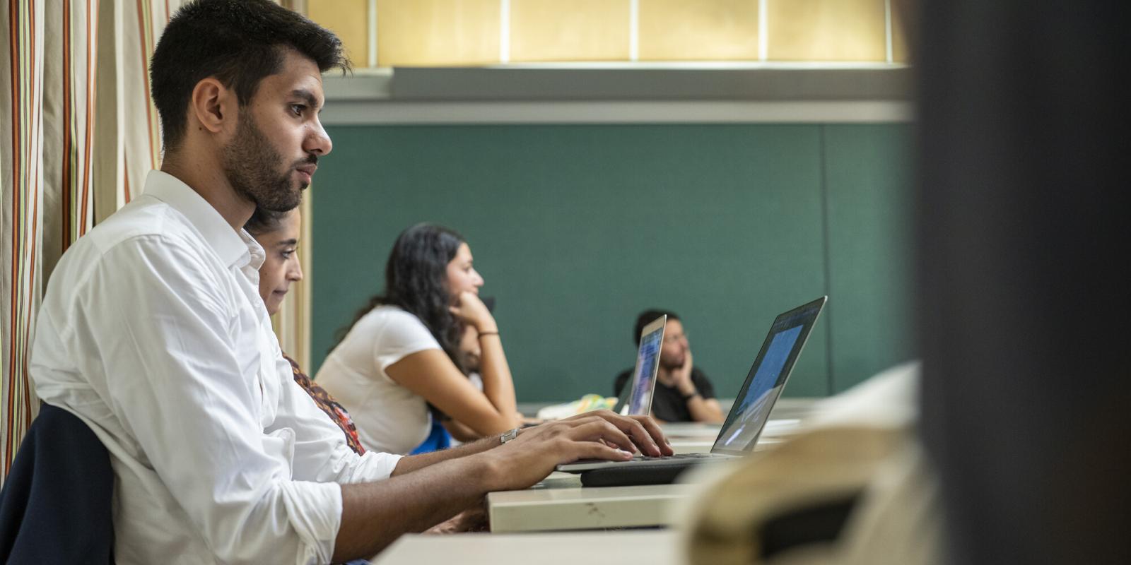 male student in class taking notes on laptop