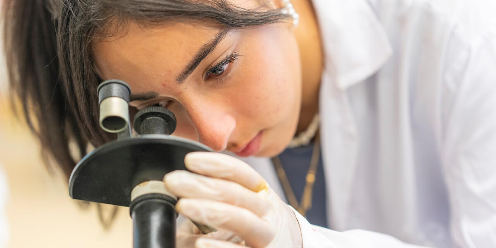 student working with microscope wearing a white lab coat