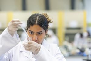 female student in lab coat working with chemical equipment in lab