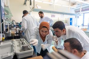 students wearing white lab coats working together on an experiment