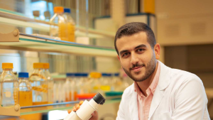 Yousef Taha in a labcoat with a hand on a microscope