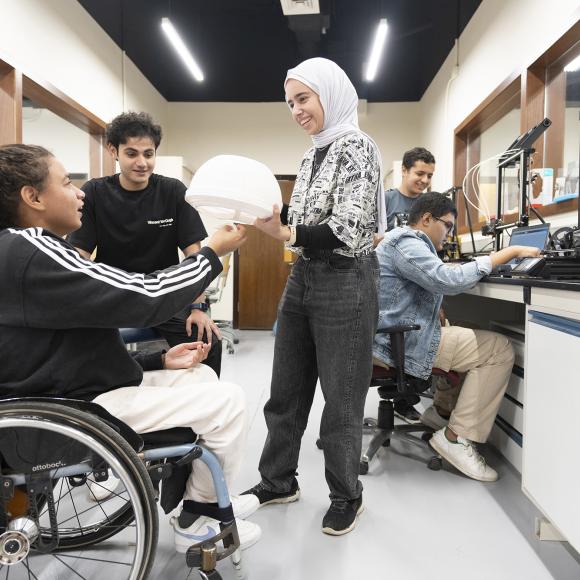 Students and student with a wheel chair at the learning factory lab using equipment