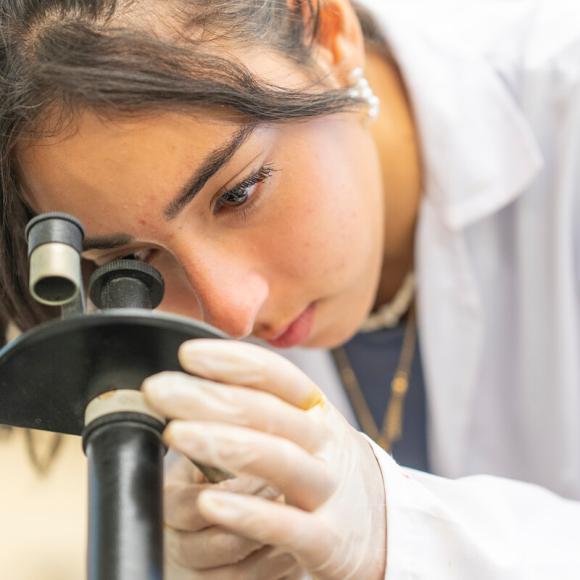 student working with microscope wearing a white lab coat